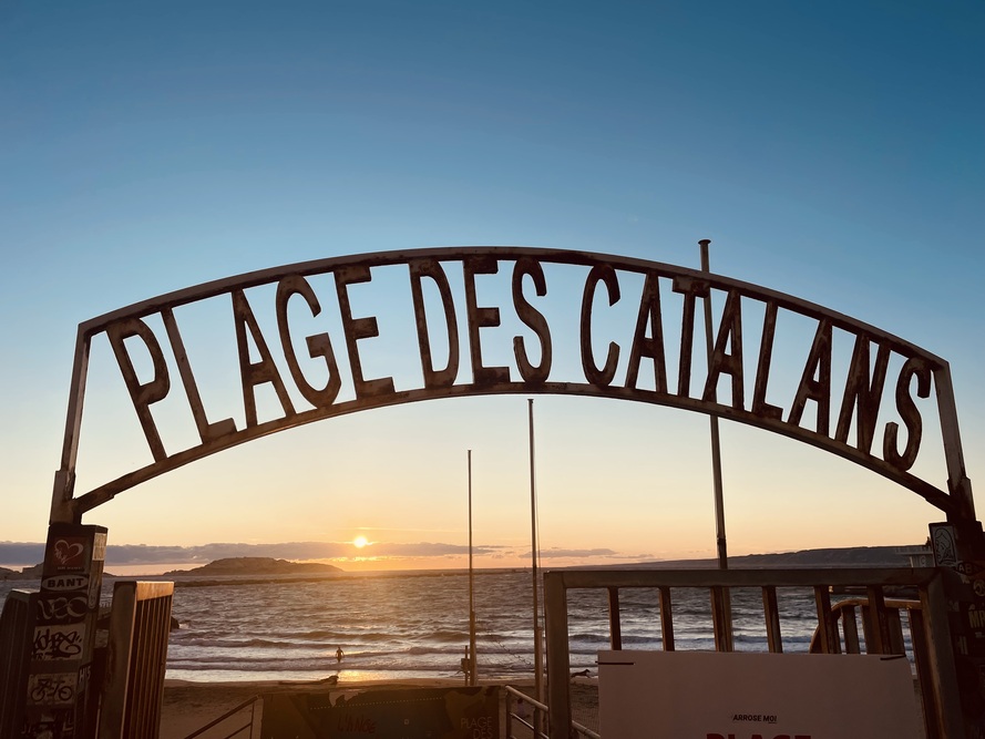 Eingangstor zum Plage des Catalans in Marseille bei Sonnenuntergang – Blick auf Meer, Wellen und Inseln im Licht
