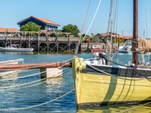 Gelbes Boot im Bassin d’Arcachon vor Austernhütten und Holzsteg