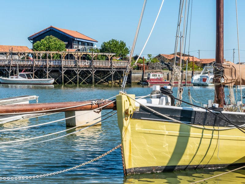 Gelbes Boot im Bassin d’Arcachon vor Austernhütten und Holzsteg